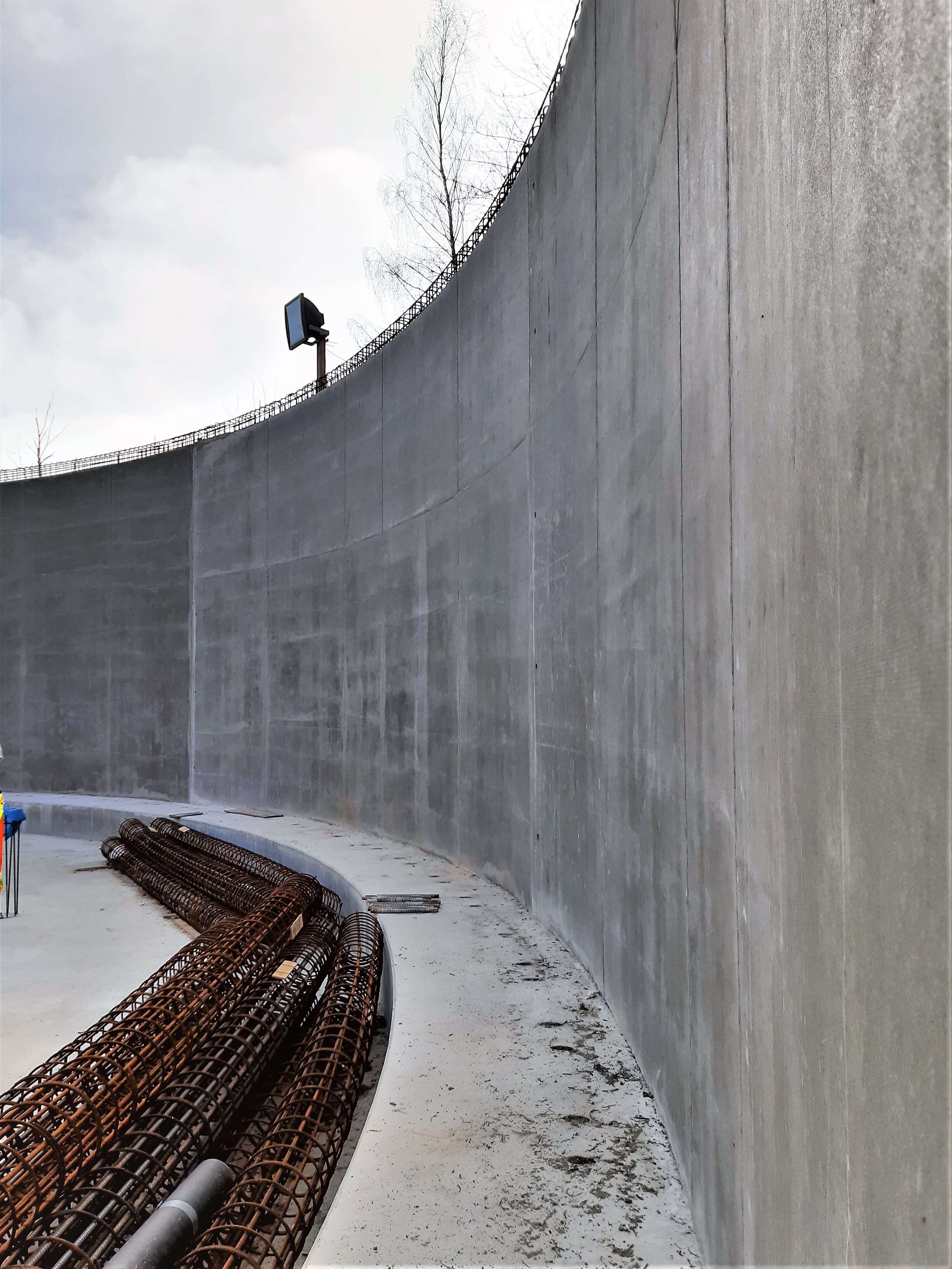 Ein großer Teil der Wandfläche ist fertiggestellt. Im Vordergrund liegen die Bewehrungskörbe für die Deckenstützen bereit.